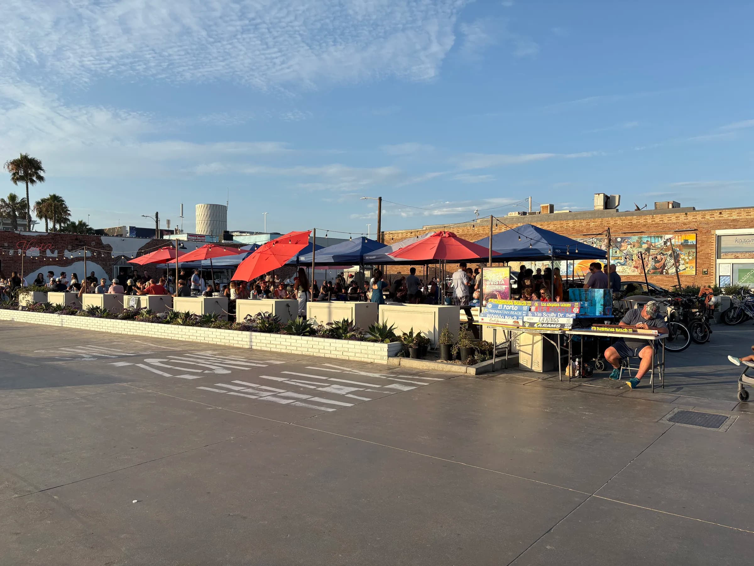 A local artist painting Hermosa Beach signs beside a lively outdoor gathering