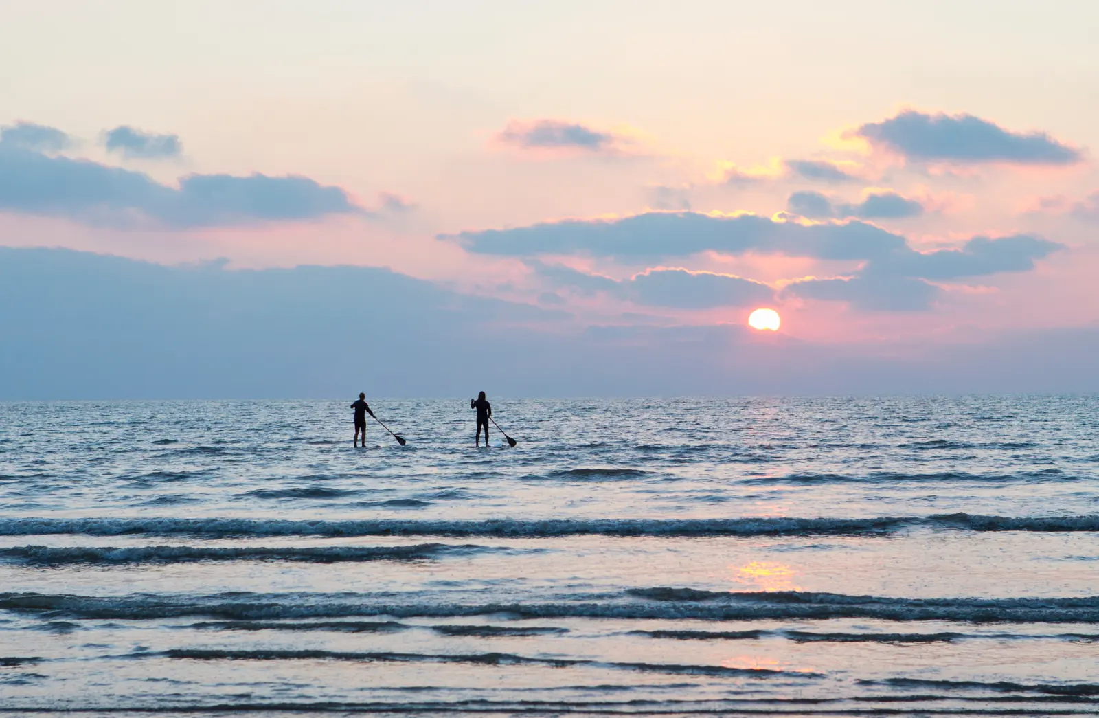 A couple paddleboarding together at sunset