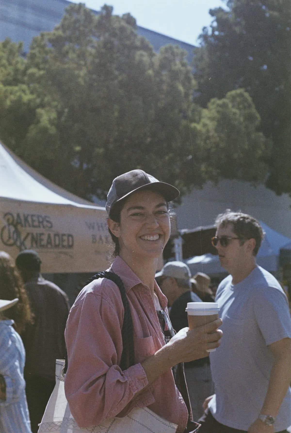 A smiling shopper holding coffee at a neighborhood farmers market