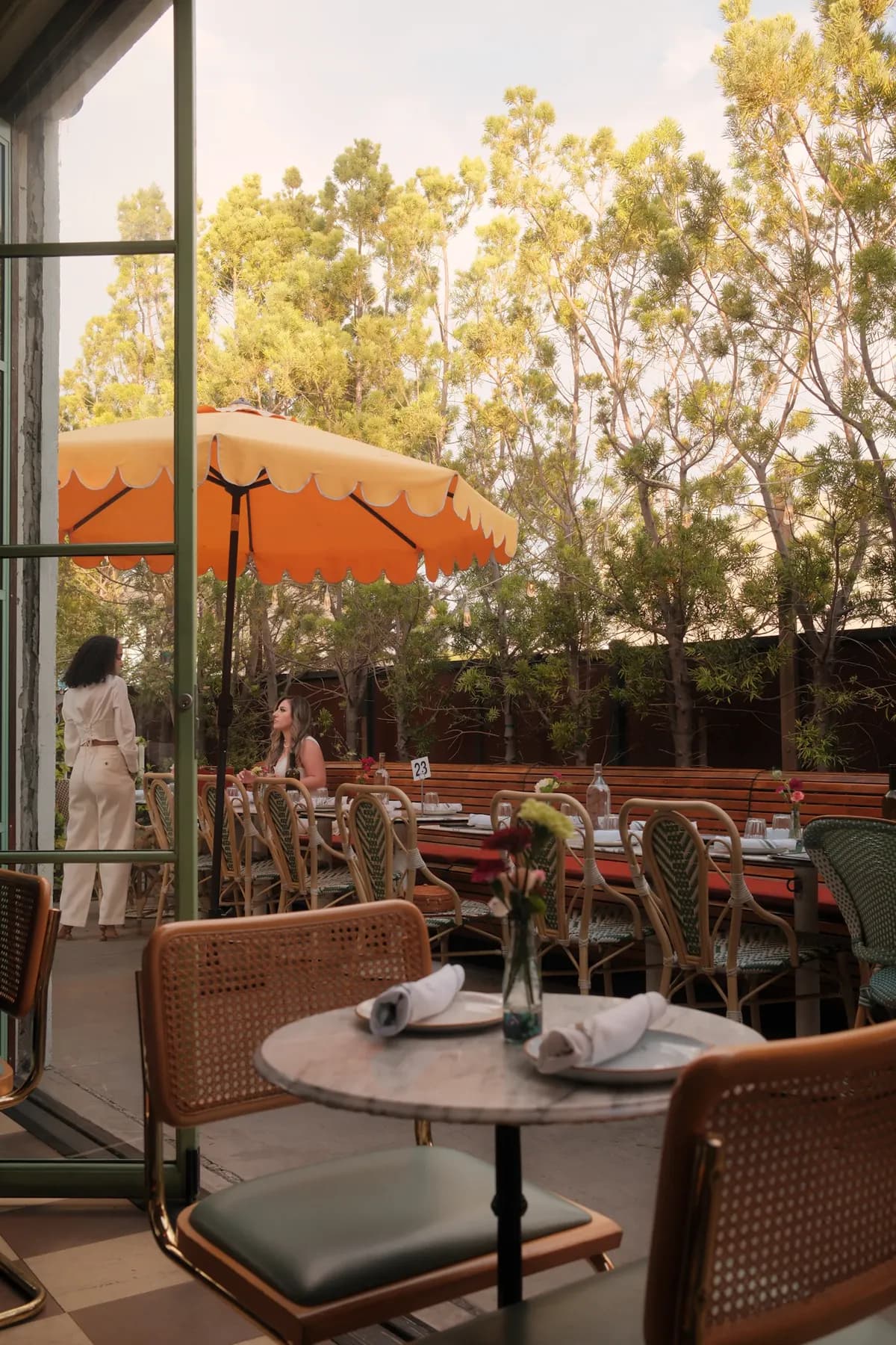 Diners gathering beneath umbrellas on a leafy Los Angeles restaurant patio