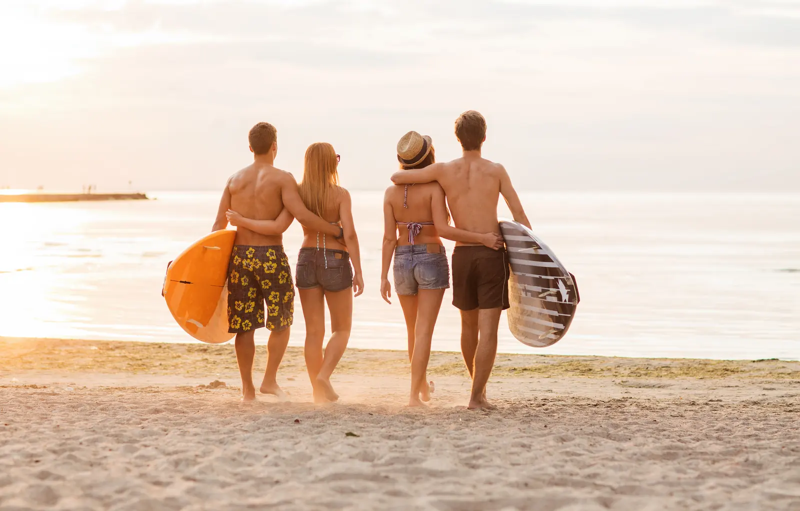Surfer friends carrying their boards along a sandy shoreline