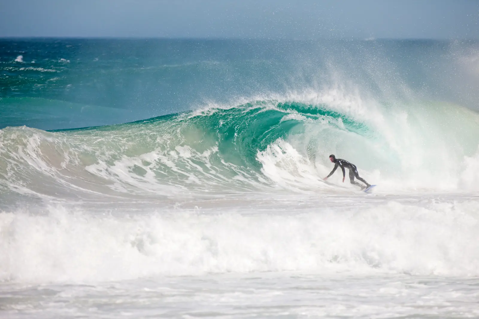 A surfer riding through the curl of a blue wave