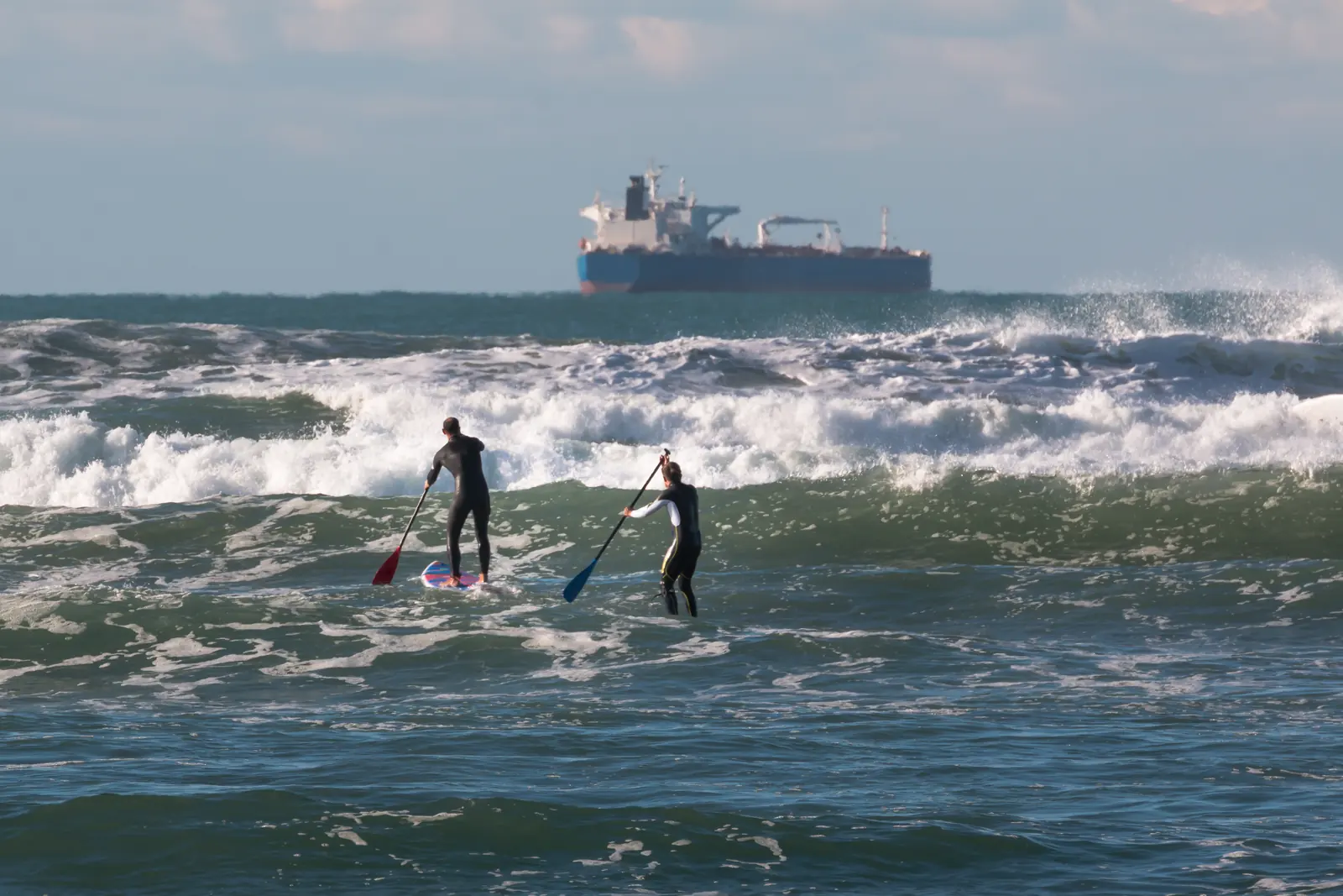 Two paddleboarders moving through open ocean waves