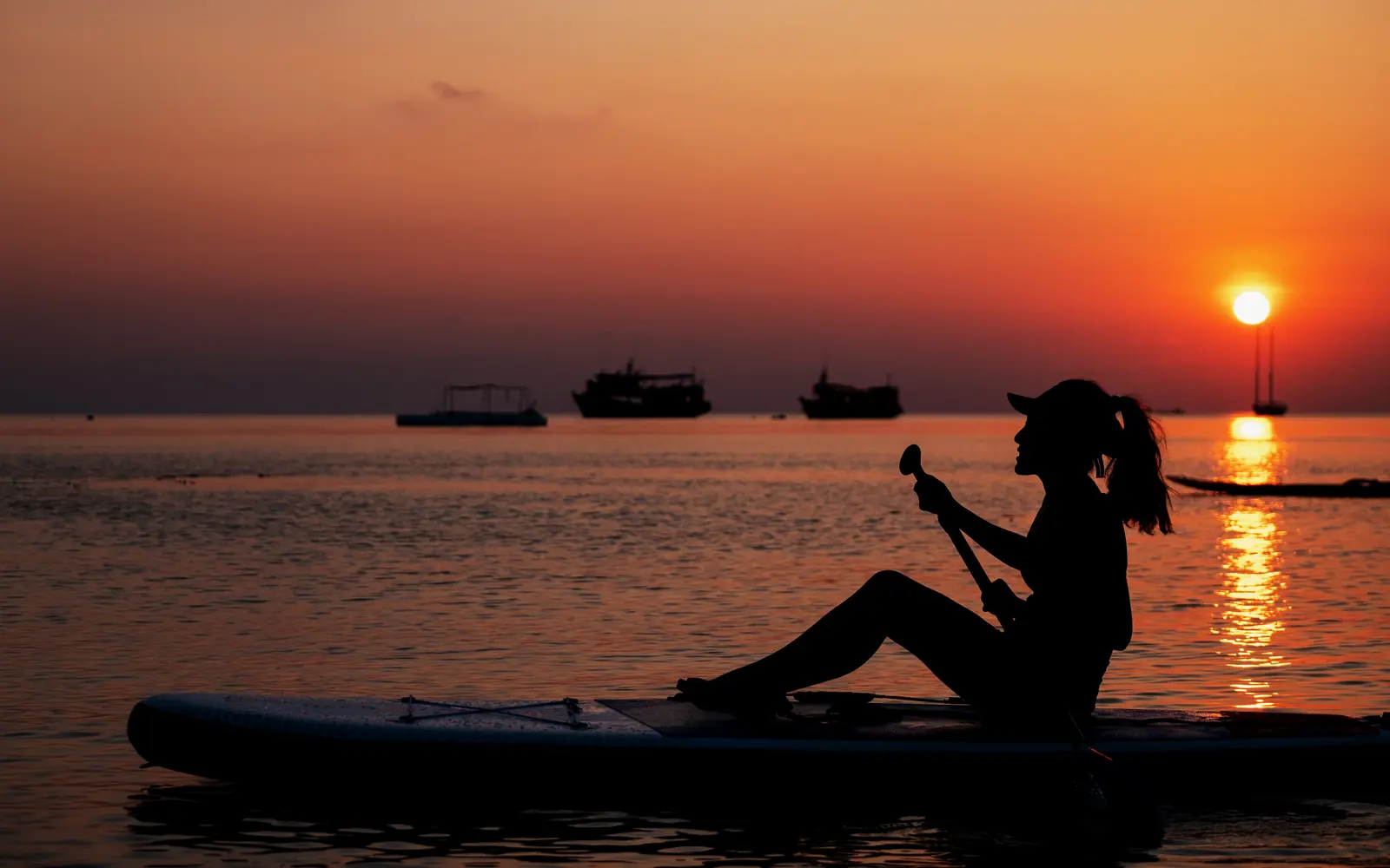 A paddleboarder moving across the water at sunset