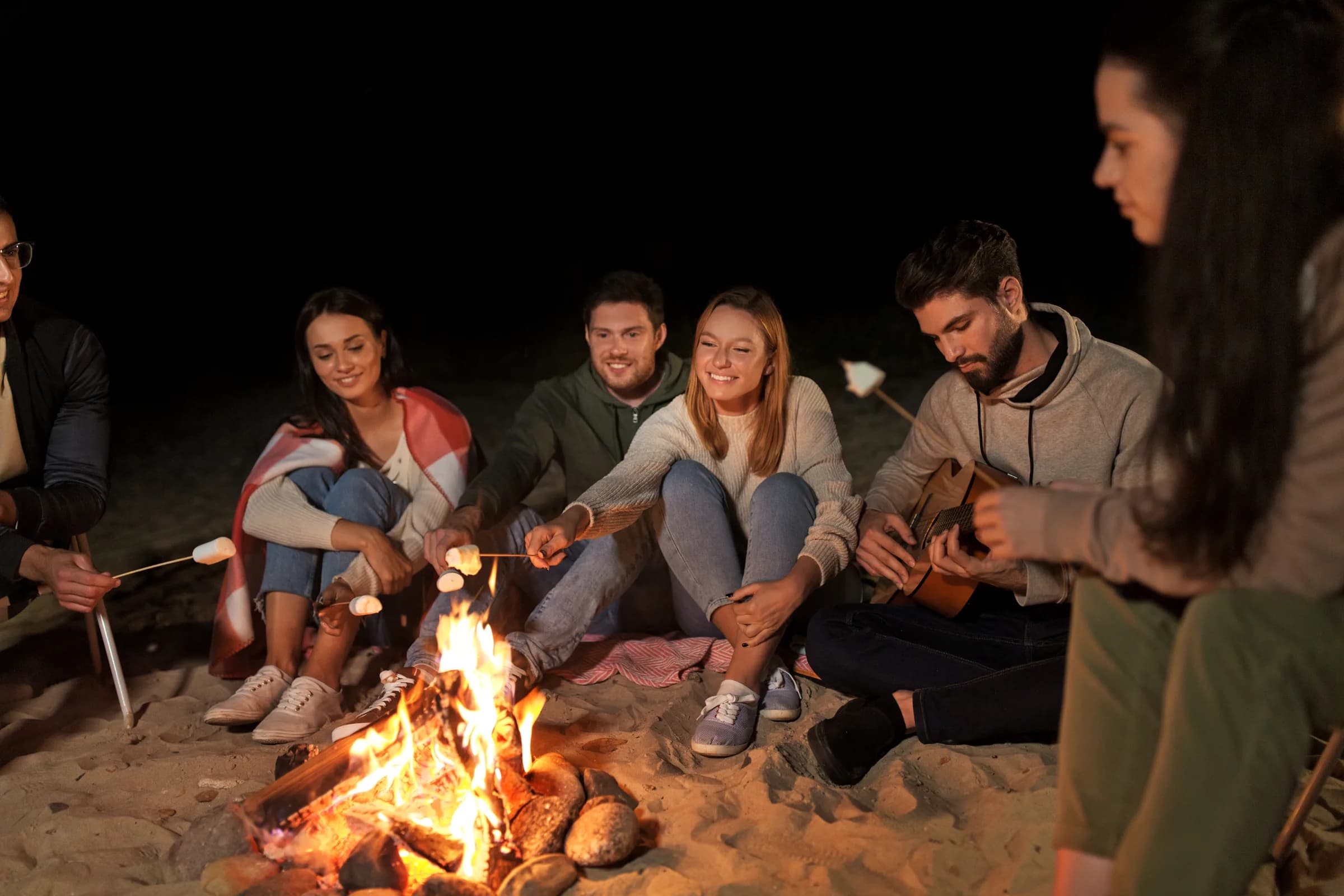Friends gathered around a bonfire on a flat sandy beach