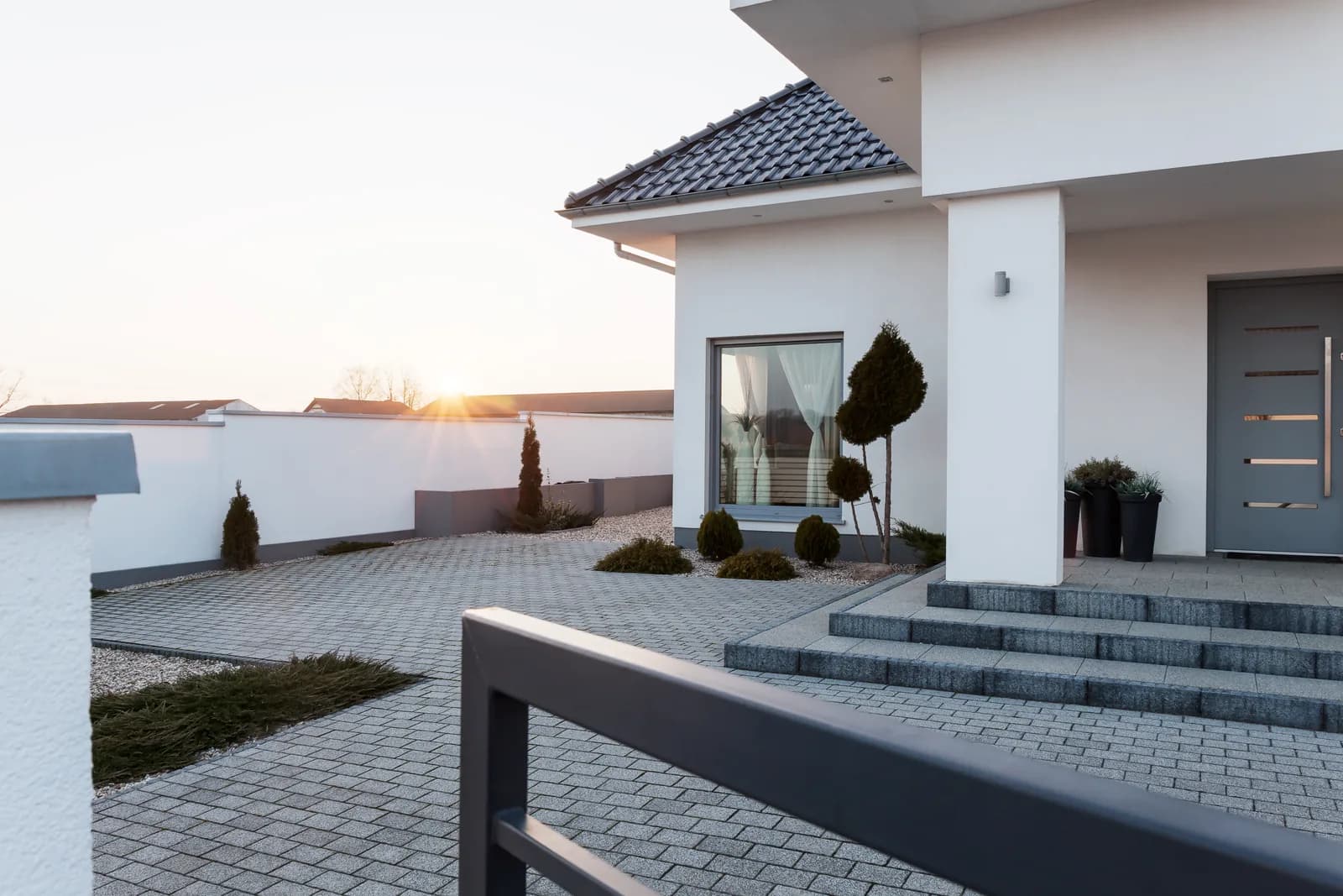 A modern white residence surrounding a broad paved courtyard at sunset