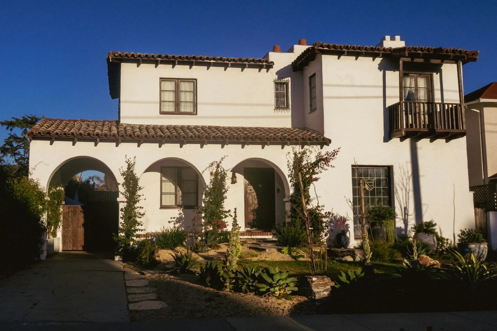 A white Spanish-style home with an arched entry and tiled roof